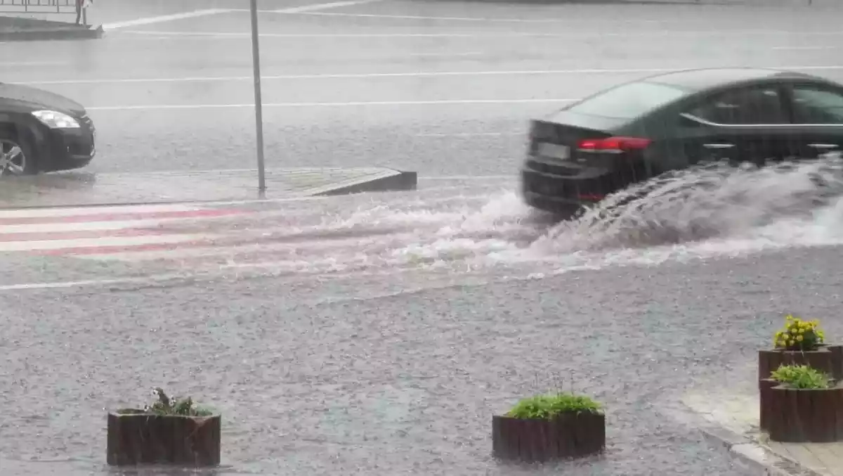 Dos coches levantando agua del suelo al pasar por charcos mientras circulan.
